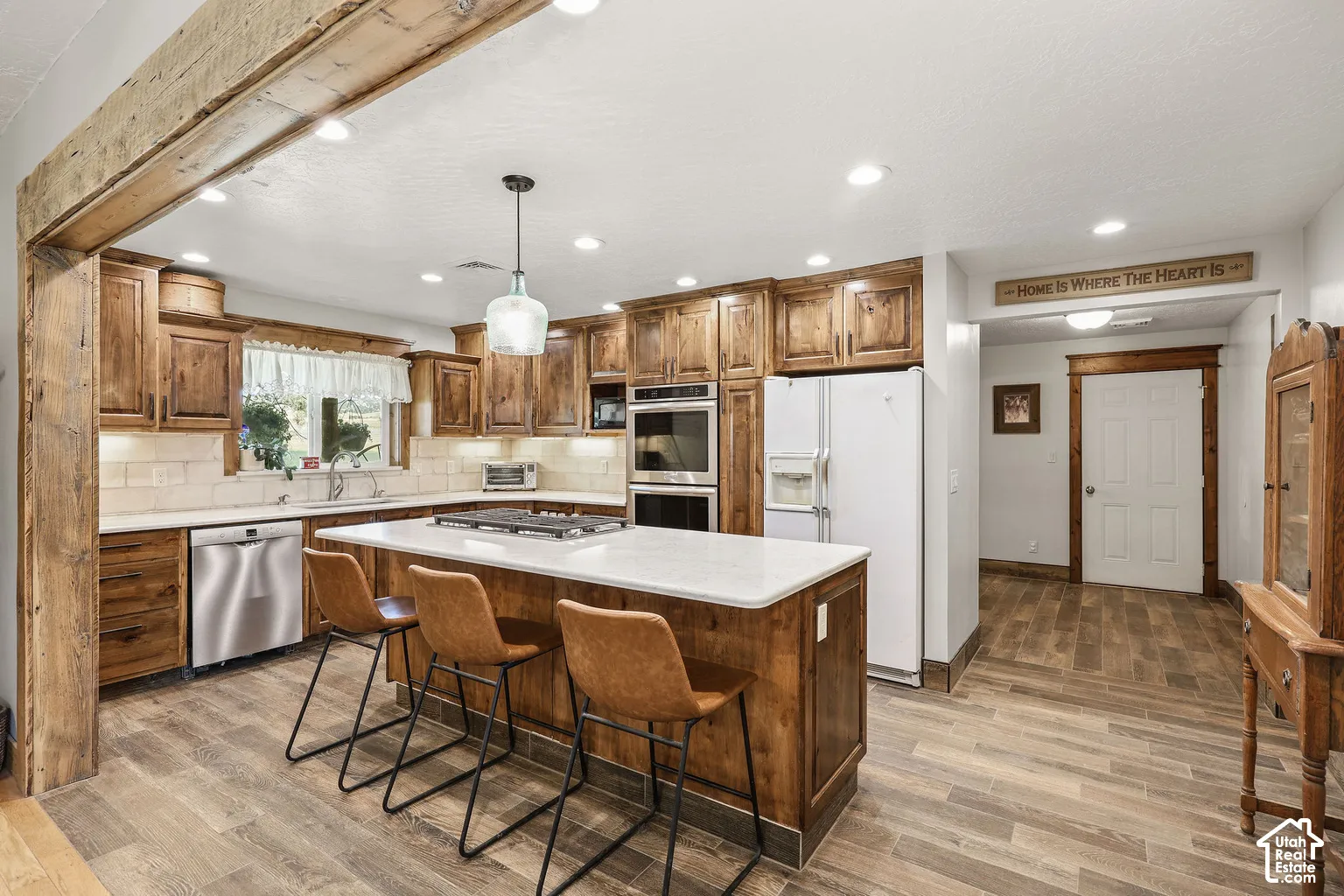Kitchen featuring custom knotty wood cabinetry, quartz countertops, built-in double wall ovens, recessed lighting, and a central island with an integrated cooktop
