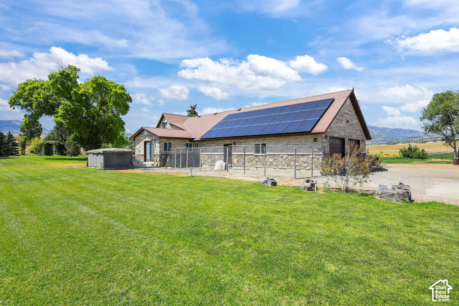Exterior featuring stone veneer siding, roof-mounted solar panels, a metal roof, and an expansive lawn