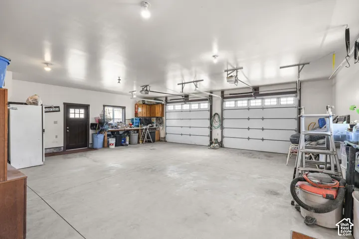 Three-car garage featuring two overhead doors, concrete flooring, built-in wooden cabinetry, and an exterior access door with glass panes