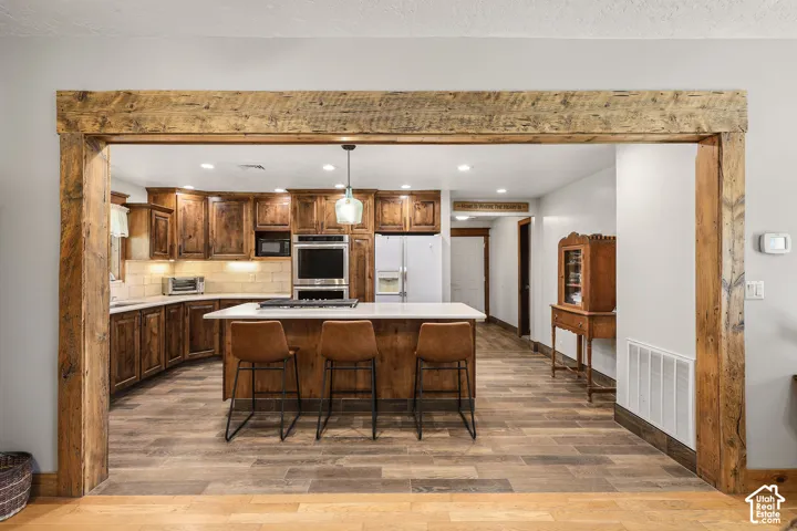 Kitchen featuring a reclaimed wood architectural beam, wood-finish flooring, custom wood cabinetry, a central island with a stone-composite countertop, and built-in double ovens