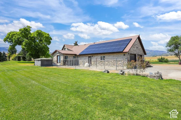 Exterior featuring stone veneer siding, roof-mounted solar panels, a metal roof, and an expansive lawn