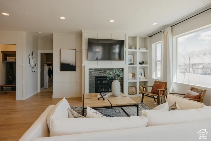 Living area featuring a fireplace with brick surround, floor-to-ceiling wainscoting, custom built-in shelving, recessed lighting, and wood-finish flooring