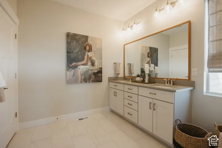 Dual-sink vanity with neutral countertop, undermount sinks, wood-framed mirror, and tiled flooring