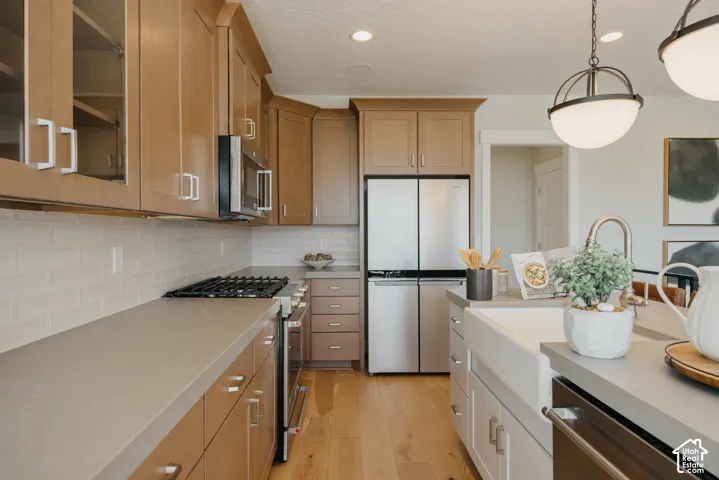 Kitchen featuring light wood-finish cabinetry, solid-surface countertops, a white porcelain apron-front sink, white subway tile backsplash, and stainless steel appliances
