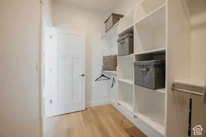 Walk-in closet featuring white custom built-in shelving, wood-finish flooring, and a multi-panel interior door