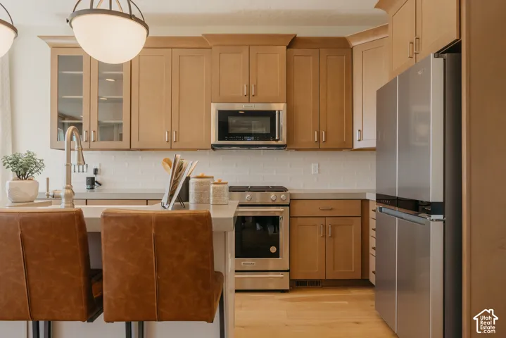 Kitchen featuring natural wood cabinetry, stainless steel appliances, subway tile backsplash, solid-surface countertops, and wood-finish flooring