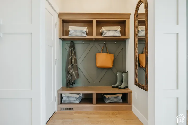 Built-in storage bench featuring wood-finish cabinetry, an olive-toned paneled accent wall with decorative millwork, upper cubbies, and metal hardware