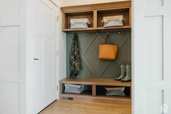 Built-in mudroom locker featuring custom wood cabinetry, upper and lower storage cubbies, decorative wall millwork, and metallic coat hooks