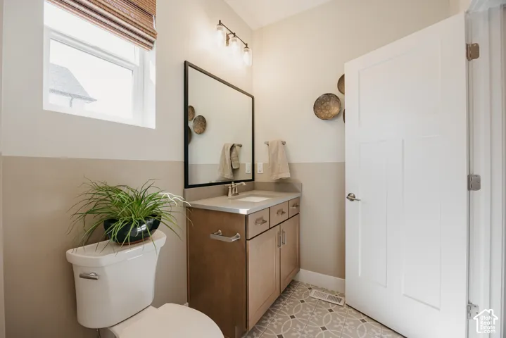 Wood cabinetry with metallic hardware, solid surface countertop, rectangular undermount sink, framed mirror, and patterned tile flooring