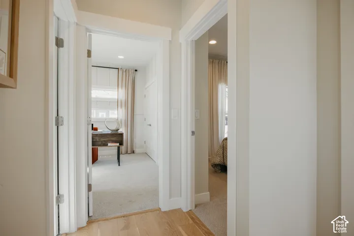 Interior hallway featuring wood-finish flooring, white door casings, recessed lighting, and neutral carpeted flooring