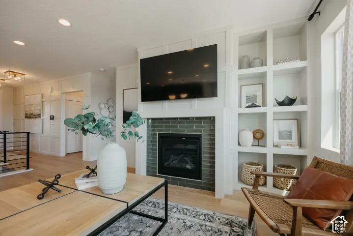Fireplace with green tiled surround, integrated white millwork shelving, grid-pattern wall molding, wood-finish flooring, and recessed ceiling lighting