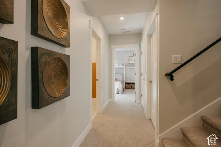 Hallway featuring neutral wall tones, carpeted flooring, white door casings, and a black metal handrail