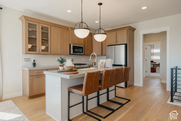 Kitchen featuring shaker-style wood cabinetry, stainless steel appliances, a central island with a quartz countertop, and dual globe pendant lighting over wood-finish flooring