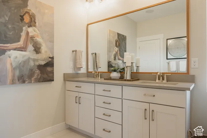 Double vanity featuring white shaker-style cabinetry, solid-surface countertops with integrated dual sinks, polished metallic hardware, and a large-format mirror with a wood-finish frame