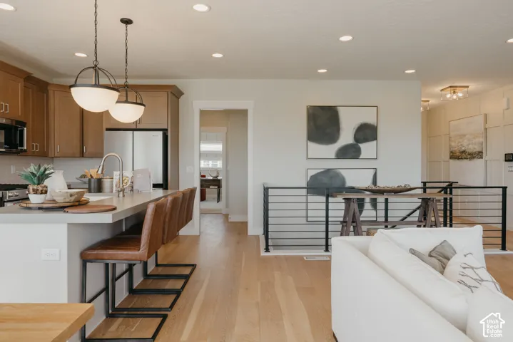 Kitchen featuring wood-finish cabinetry, an expansive island with a solid-surface countertop, recessed lighting, pendant fixtures, and wood-finish flooring with a modern horizontal-rail staircase