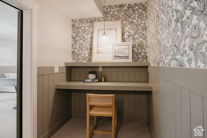 Built-in desk with a solid surface countertop, vertical wood-panel wainscoting, decorative patterned wallpaper, and a suspended pendant light fixture