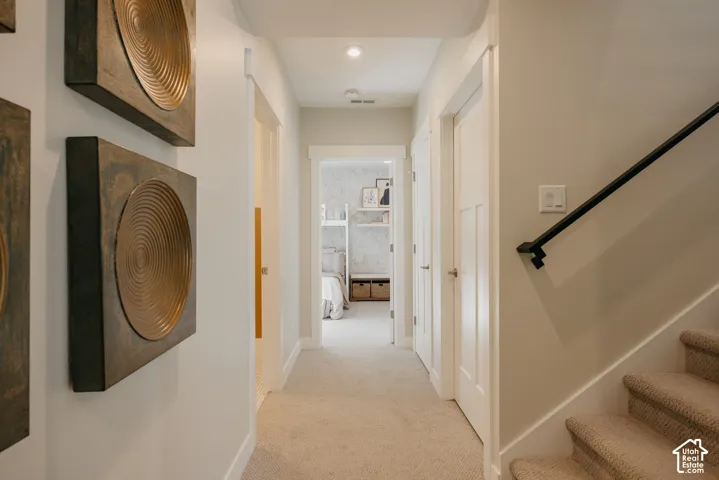 Hallway featuring neutral-toned carpeting, white shaker-style interior doors, recessed ceiling lighting, and a staircase with a matte black metal handrail