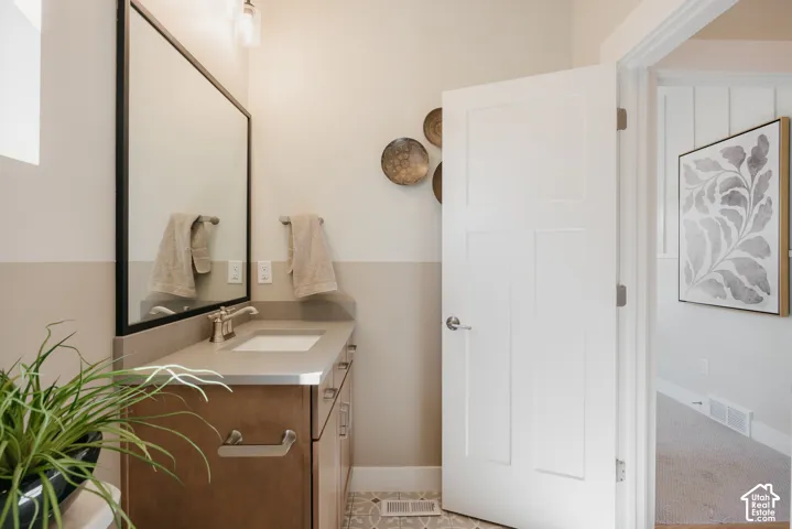 Wood cabinetry, solid-surface countertop with an integrated rectangular sink, wall-mounted mirror with a black frame, brushed-nickel faucet, and patterned tile flooring