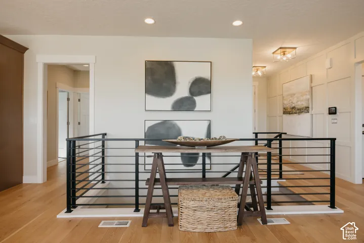 Interior space featuring wood-finish flooring, custom wall paneling with geometric detailing, recessed lighting, and a modern black metal railing