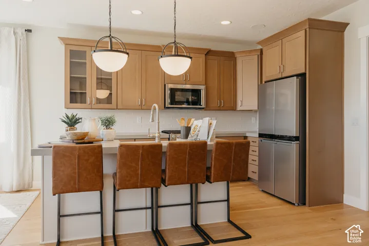 Kitchen featuring wood cabinetry, subway tile backsplash, stainless steel appliances, central island with sink, and wood-finish flooring