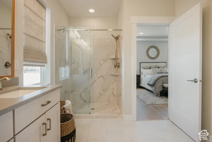 Bathroom featuring a walk-in shower with floor-to-ceiling stone-patterned tile, frameless glass sliding door, vanity with solid-surface countertop, and large-format porcelain floor tile