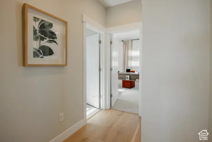 Interior hallway featuring light-toned wood-finish flooring, crisp neutral wall paint, and white multi-panel interior doors with matching casing