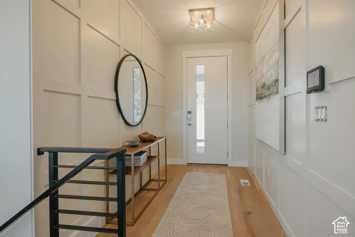 Entryway featuring grid-pattern wall molding, light wood-finish flooring, a white paneled door with a vertical glass inset, and a modern geometric ceiling light fixture