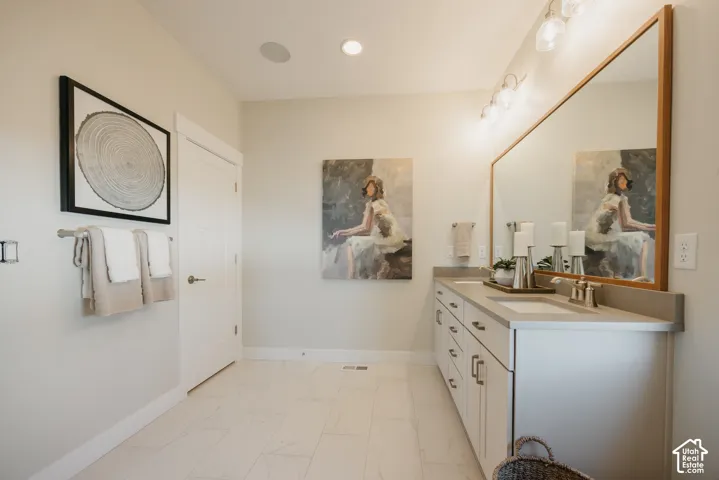 Dual-sink vanity with stone-finish countertop, full-width wood-framed mirror, undermount sinks, and tiled flooring
