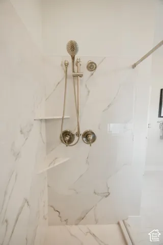 Shower enclosure featuring large-format tile with veining, built-in corner shelving, a sliding hand-held shower head, and dual circular control valves with a brushed nickel finish