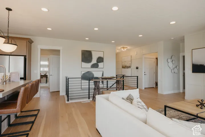 Open-concept interior featuring light wood-finish flooring, recessed lighting, matte black metal horizontal stair railing, and wall paneling