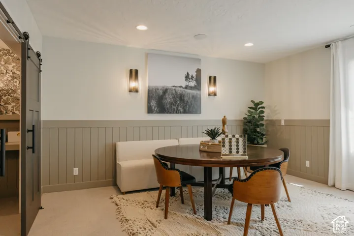 Interior space featuring vertical wood wainscoting, sliding barn door with matte black hardware, recessed ceiling lighting, and wall-mounted metal sconces