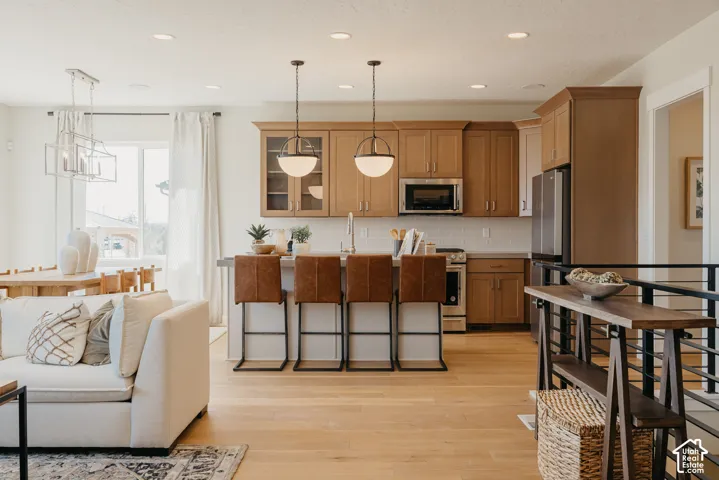 Kitchen featuring light wood-finish cabinetry, a white tile backsplash, a center island with pendant lighting, and recessed ceiling lights, all complemented by wood-finish flooring