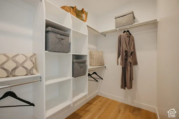 Walk-in closet featuring white built-in shelving, integrated hanging rods, and wood-finish flooring
