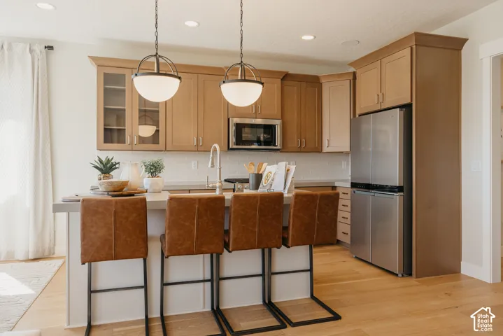 Kitchen featuring light-tone cabinetry, stainless steel appliances, a central island with countertop seating, recessed lighting, and pendant fixtures