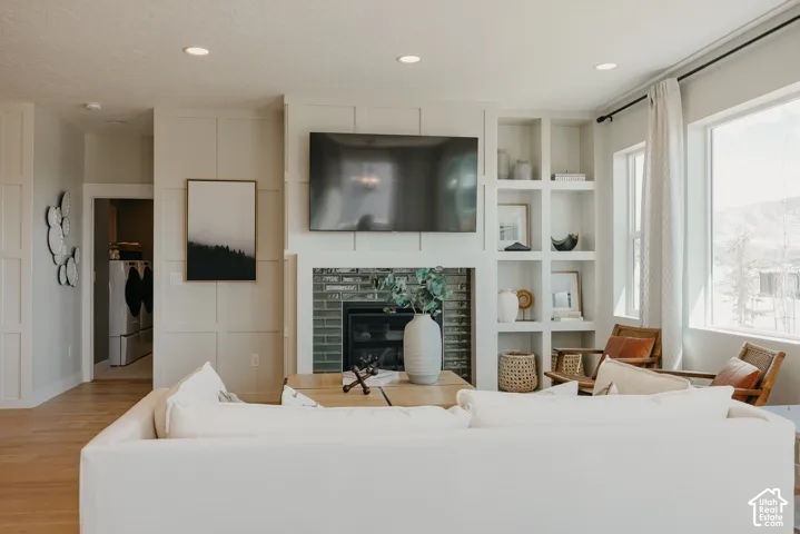 Living area featuring a floor-to-ceiling wainscoting accent wall, built-in shelving, a fireplace with a multi-toned tile surround, wood-finish flooring, and recessed lighting