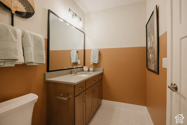 Vanity featuring a solid-surface countertop with an integrated rectangular sink and wood-finish cabinetry, paired with a large rectangular mirror, three-light fixture, and ceramic tile flooring