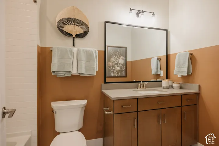 Bathroom featuring a vanity with shaker-style cabinetry, solid-surface countertop, rectangular undermount sink, framed wall-mounted mirror, and a three-bulb light fixture