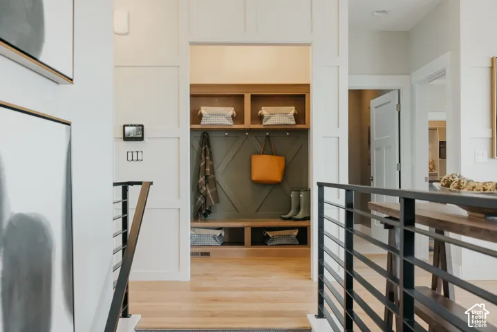Built-in mudroom nook with wood-finish shelving and bench seating, framed by white board-and-batten wall paneling and metal horizontal-bar railing