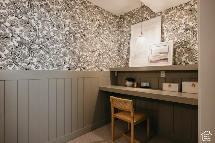 Built-in desk with integrated shelving, vertical plank wall paneling, patterned wallpaper, and a suspended pendant light fixture