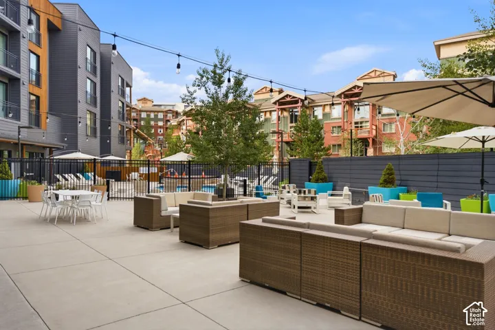 Outdoor courtyard featuring concrete paving, string lighting, decorative planters, and perimeter metal fencing