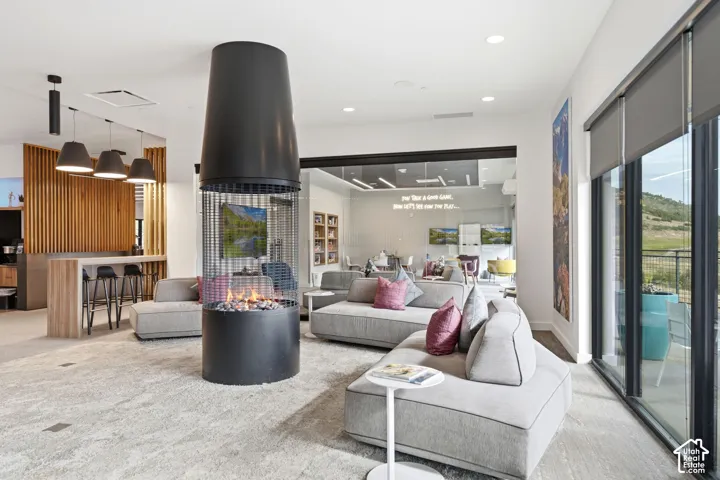 Freestanding cylindrical metal fireplace with glass-enclosed hearth, recessed ceiling lighting, wood-slat accent wall, and expansive floor-to-ceiling glass paneling