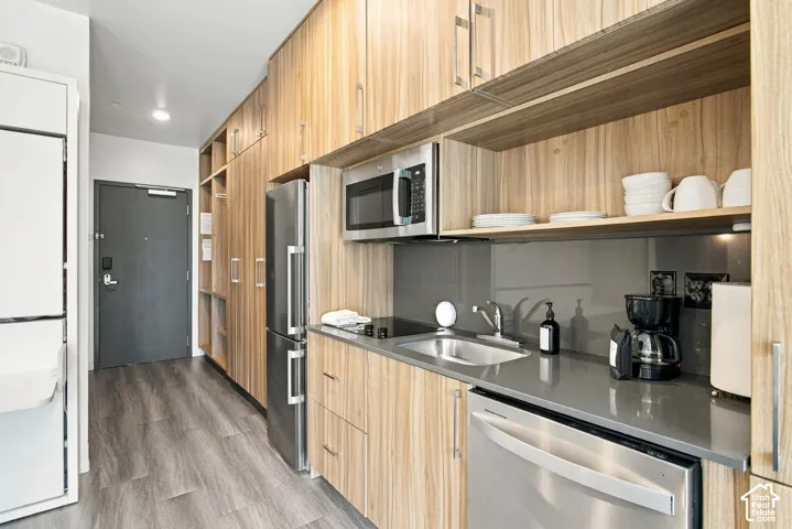 Kitchenette featuring wood-finish cabinetry, gray solid-surface countertops, a glass-surface cooktop, stainless steel appliances, and a gray glass backsplash