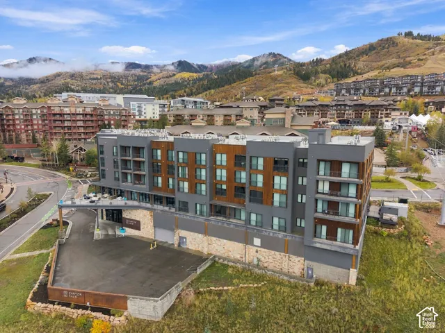 Multi-story building exterior featuring dark gray metal panels, wood-finish siding, stone foundation masonry, and multiple private balconies with mountain backdrop