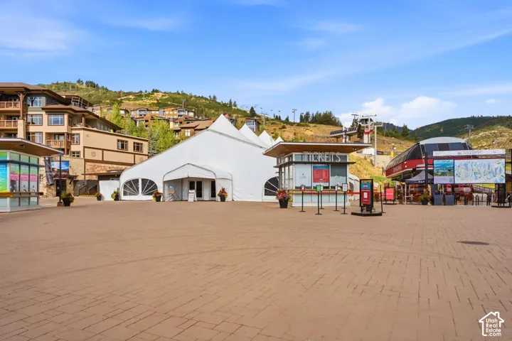 Expansive paved plaza featuring integrated mountain resort infrastructure, including ski lift access points and ticketing kiosks set against a backdrop of mountainous terrain