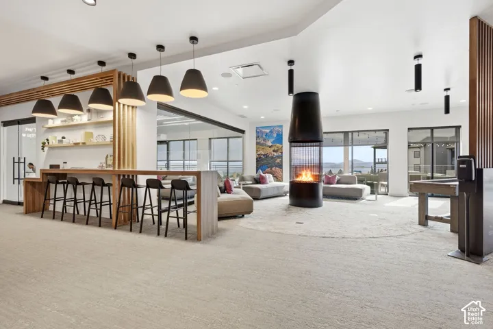 Open-concept interior featuring a central floor-to-ceiling metal fireplace, custom wood slat divider wall, built-in bar-style counter, industrial-style pendant lighting, and large windows
