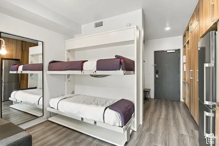 Built-in white wall-mounted bunk unit, full-length wall mirror, extensive wood-finish cabinetry, wood-finish flooring, and stainless steel kitchen appliances