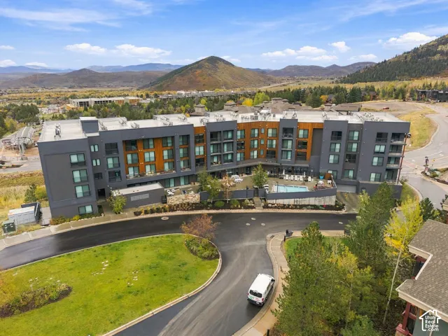 Multi-story building with dark siding, wood-toned paneling, private balconies, an on-site swimming pool, and mountain scenery