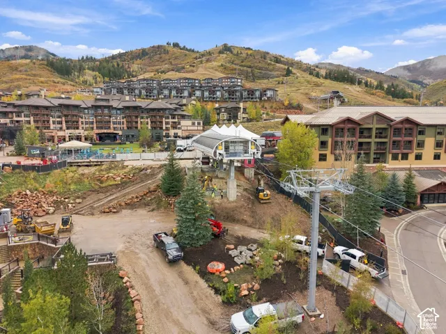Mountain landscape featuring a ski lift infrastructure, multi-story commercial buildings with brown wood-tone siding, and stone retaining walls amidst evergreen and aspen trees