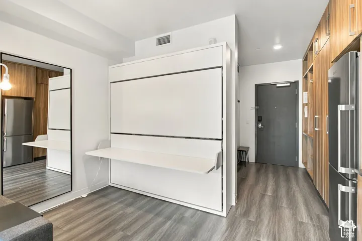 Built-in wall unit featuring a white fold-down desk, full-height wood-finish cabinetry, stainless steel refrigerator, and wood-finish flooring