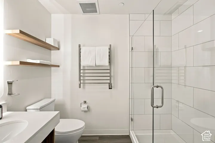 Walk-in shower with floor-to-ceiling white subway tile, frameless glass enclosure, wood-finish shelving, and wall-mounted stainless steel towel warmer